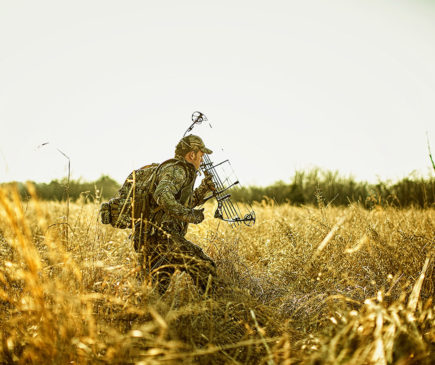 hunter walking through a field with a crossbow